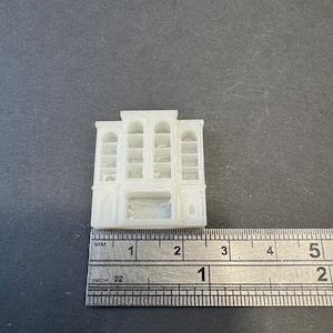 May include: White 3D printed model of a building with multiple windows and a storefront. The model is approximately 1.5 inches tall and 1 inch wide.