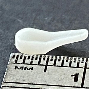 Puede incluir: Un pequeño puente nasal para gafas de plástico blanco, que mide aproximadamente 1 cm de largo, se muestra junto a una regla.