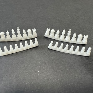 May include: Four rows of white plastic chess pieces, including pawns, rooks, knights, bishops, queens, and kings. The pieces are arranged in rows on a gray surface.