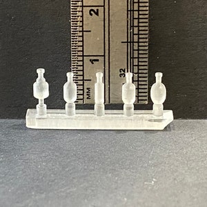Peut inclure: Un grappe en plastique transparent avec cinq composants miniatures en forme de bouteille. Une règle en millimètres est positionnée derrière les composants. Les bouteilles varient en forme.