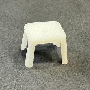 Könnte beinhalten: Ein kleiner, weißer Plastiktisch mit quadratischer Platte und vier Beinen.