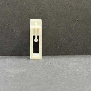 以下が含まれることがあります： 黒い開口部のある白いプラスチック製のカーテンクリップ。クリップには、開口部の真ん中に小さな黒い円があります。