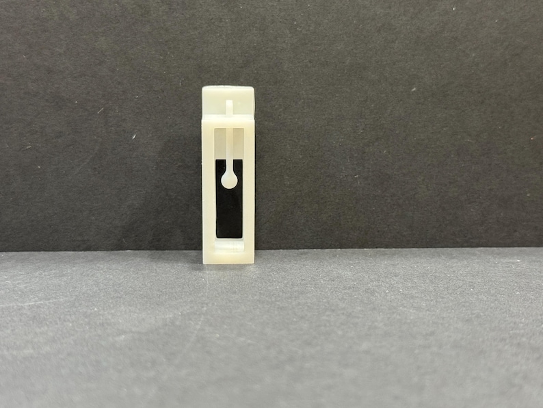 以下が含まれることがあります： 黒い開口部のある白いプラスチック製のカーテンクリップ。クリップには、開口部の真ん中に小さな黒い円があります。