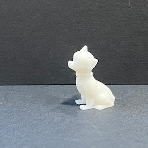 May include: A white ceramic figurine of a small dog sitting with its head tilted up. The dog has a smooth, glossy finish.