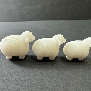 May include: Three white sheep figurines, each with a different size. The sheep are made of a textured material that resembles wool.