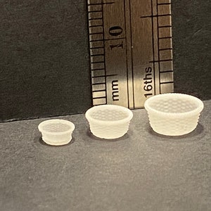 May include: Three white plastic baskets of varying sizes. The baskets have a woven pattern and are ideal for miniature dollhouse decor.