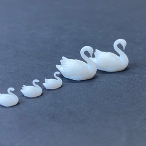 Puede incluir: Un conjunto de seis figuras de cisnes blancas, dispuestas en orden de tamaño, de la más pequeña a la más grande. Los cisnes están hechos de un material blanco liso y tienen un aspecto realista.