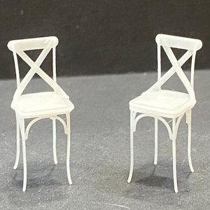 May include: Two white wooden chairs with a cross-shaped back design. The chairs have a simple, minimalist style.