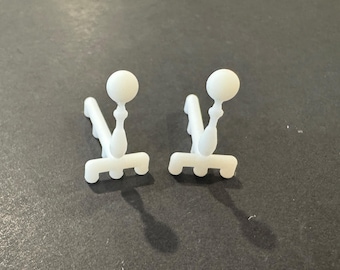 Könnte beinhalten: Zwei kleine, weiße Kunststoffobjekte mit einem einzigartigen Design. Jedes hat eine abgerundete Oberseite, einen schlanken Stiel und eine dreizackige Basis. Die Objekte befinden sich vor einem dunklen Hintergrund und werfen Schatten.