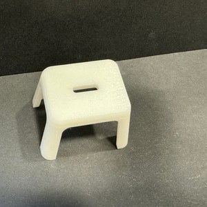 Pode incluir: Um banquinho de plástico branco com um pequeno recorte retangular na parte superior.
