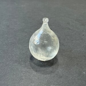 May include: A clear glass bottle with a round body and a narrow neck. The bottle has a textured surface.