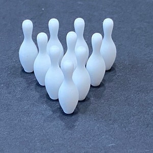 May include: A set of ten white bowling pins arranged in a triangle formation on a dark gray surface.