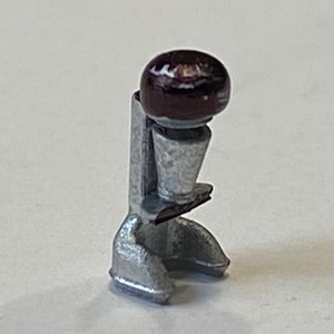 May include: A silver metal stand with a round, dark brown top. The stand has a textured surface and a unique design.