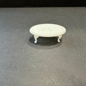 Könnte beinhalten: Weißer ovaler Tisch mit vier Beinen. Der Tisch ist aus glattem, weißem Material gefertigt und hat ein schlichtes, elegantes Design.
