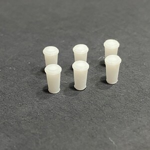 Peut inclure: Sept gobelets en plastique blanc disposés de manière symétrique sur une surface gris foncé.