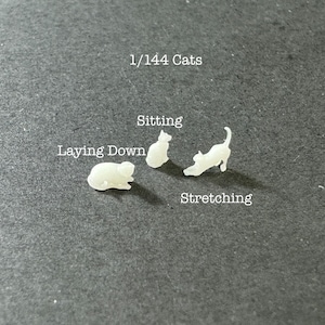 May include: Four white plastic cat figurines in different poses: sitting, laying down, and stretching. The figurines are labeled "1/144 Cats", "Sitting", "Laying Down", and "Stretching".