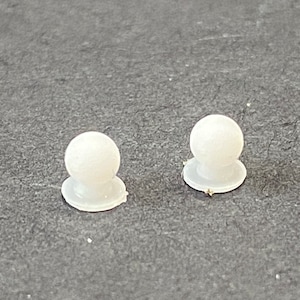 May include: Two white plastic buttons with a round top and a flat base.