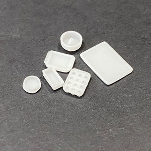 May include: A set of six white plastic kitchen molds, including a round mold, a rectangular mold, a square mold, and a mold with multiple small circles. The molds are on a dark gray surface.