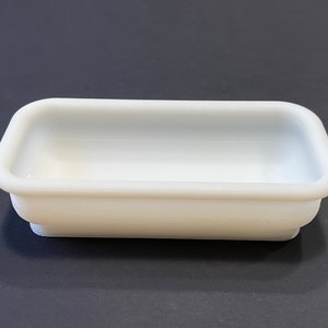 May include: A white rectangular ceramic dish with a smooth, glossy finish. The dish has a slightly rounded bottom and a wide, shallow interior.