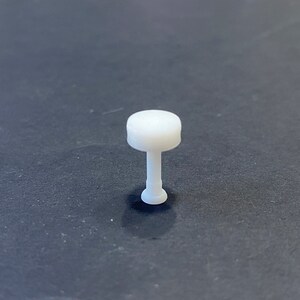 Könnte beinhalten: Eine weiße Plastik-Reißzwecke mit einem runden Kopf und einem zylindrischen Schaft.