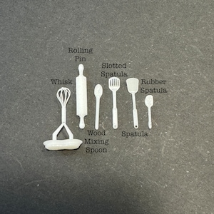 Puede incluir: Un juego de utensilios de cocina de plástico blanco, que incluye un batidor, un rodillo, una espátula ranurada, una espátula, una espátula de goma y una cuchara de madera para mezclar.