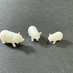 May include: Three white plastic pig figurines of varying sizes. The largest pig is standing on all four legs, while the two smaller pigs are sitting.