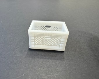 May include: A small, white, rectangular crate with a lattice design on the sides and a handle opening on the top. The crate is made of a solid material and is likely used for storage or display purposes. The crate is sitting on a dark surface.
