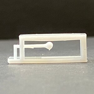以下が含まれることがあります： 透明な窓が付いた白いプラスチック製のケースで、中に小さな白い物体が表示されています。