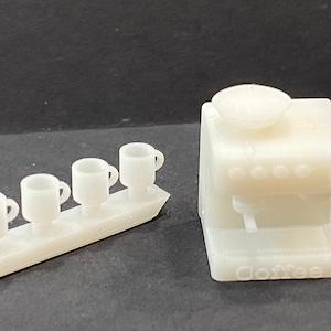 May include: White plastic miniature coffee maker with a tray of four cups. The coffee maker has the word "Coffee" printed on the front.