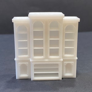 May include: A miniature white bookcase set with three connected units. The central unit has arched glass doors and shelves, flanked by two similar units. The bottom features a small open shelf and decorative panels.