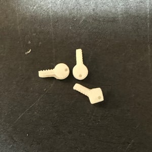May include: Three white plastic keys with round keyholes. The keys are on a dark gray surface.