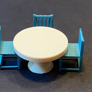 May include: A white round table with a white pedestal base and three blue chairs. The chairs have a simple design with vertical slats.