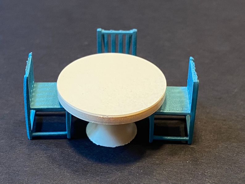 May include: A white round table with a white pedestal base and three blue chairs. The chairs have a simple design with vertical slats.