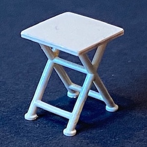 May include: White folding stool with a square seat and a simple, sturdy design.