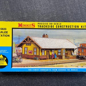 Puede incluir: Una caja de kit de tren modelo que presenta la estación Arlee amarilla, un kit de construcción de vías a escala HO precisa. La caja incluye el texto "MINIKITS" y "THE FINEST HOBBYKITS FROM AROUND THE WORLD".