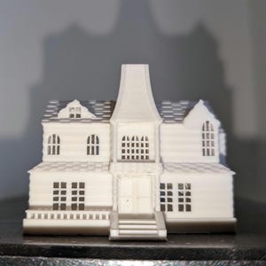 May include: A white, miniature model of a Victorian-style house. The house features multiple windows, a detailed roof, and a central tower. The model has a detailed facade with a front porch and steps leading to the front door. The overall design is intricate and detailed.