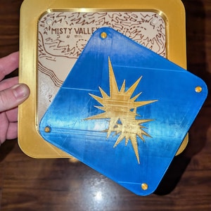 May include: A gold-colored rectangular frame with a map inside, and a blue diamond-shaped piece with a gold starburst design. The map reads "Misty Valley".