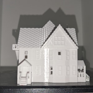 Peut inclure: Maquette blanche d'une maison avec un toit d&eacute;taill&eacute;, des fen&ecirc;tres et un porche. La maison est une r&eacute;plique miniature, mettant en valeur les d&eacute;tails architecturaux. Le mod&egrave;le est pos&eacute; sur un fond neutre.