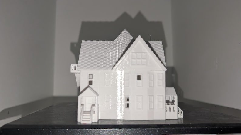 Peut inclure: Maquette blanche d'une maison avec un toit d&eacute;taill&eacute;, des fen&ecirc;tres et un porche. La maison est une r&eacute;plique miniature, mettant en valeur les d&eacute;tails architecturaux. Le mod&egrave;le est pos&eacute; sur un fond neutre.