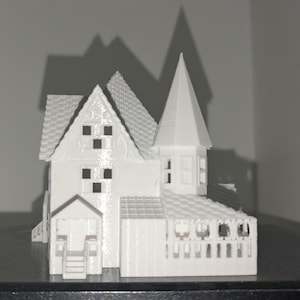 Peut inclure: Mod&egrave;le imprim&eacute; en 3D d'une maison blanche avec des d&eacute;tails complexes. La maison pr&eacute;sente un toit &agrave; pignon, une tour avec un sommet pointu et un porche. Le mod&egrave;le est pos&eacute; sur un fond uni, avec des ombres cr&eacute;ant de la profondeur.