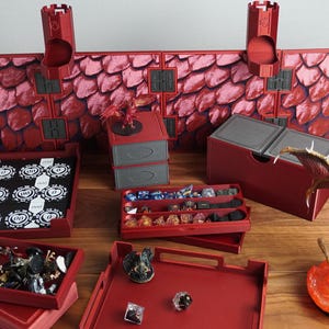 Könnte beinhalten: Eine Sammlung roter und grauer Tabletop-Gaming-Zubehörteile, darunter Würfelablagen, eine Wand im Drachen-Design und eine Drachenfigur. Das Set enthält Ablagen für Würfel, Miniaturen und Spielchips.
