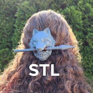 Puede incluir: Una pinza para el pelo de plata con forma de cabeza de lobo con un diseño de lanza. La pinza está en el pelo de una persona con el pelo largo y castaño. El texto "STL" es visible debajo de la pinza.