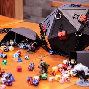 May include: A black, geometric dice bag and dice set, with a large D20 bag and a smaller dice tray. The D20 bag has red accents and a chain strap. Assorted colorful dice and miniature figurines are scattered around the bags on a wooden surface.