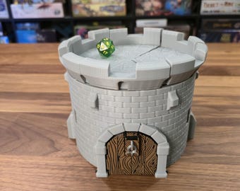 May include: A gray 3D-printed dice tower shaped like a castle turret. The tower has a wooden door and a crenelated top. A green and yellow multi-sided die rests on the top of the tower. The tower is designed for tabletop gaming.