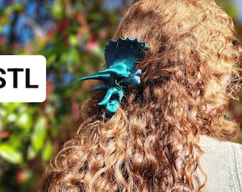 May include: A teal blue 3D printed Triceratops hair clip. The clip is in the shape of a dinosaur head with horns and a frill.