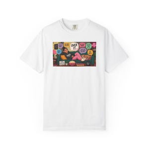 Pode incluir: Uma t-shirt branca de manga curta com uma ilustração central de uma pessoa deitada num sofá verde com um cão e um gato. O gráfico inclui vários balões de fala com texto, incluindo "OVER IT", "TOO MANY FEELINGS" e "NOT TODAY SATAN".