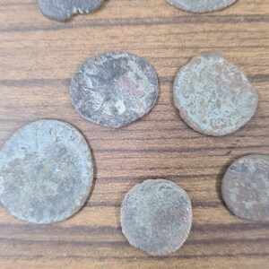 Puede incluir: Una colecci&oacute;n de ocho monedas antiguas de plata con diferentes grados de desgaste y p&aacute;tina. Las monedas est&aacute;n dispuestas sobre una superficie de madera.