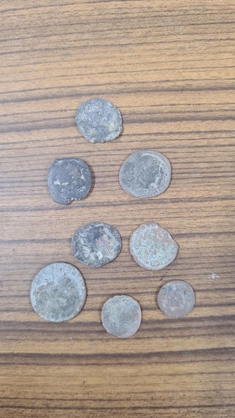 Puede incluir: Una colecci&oacute;n de ocho monedas antiguas, algunas con una p&aacute;tina verdosa, dispuestas en un patr&oacute;n triangular sobre una superficie de madera.