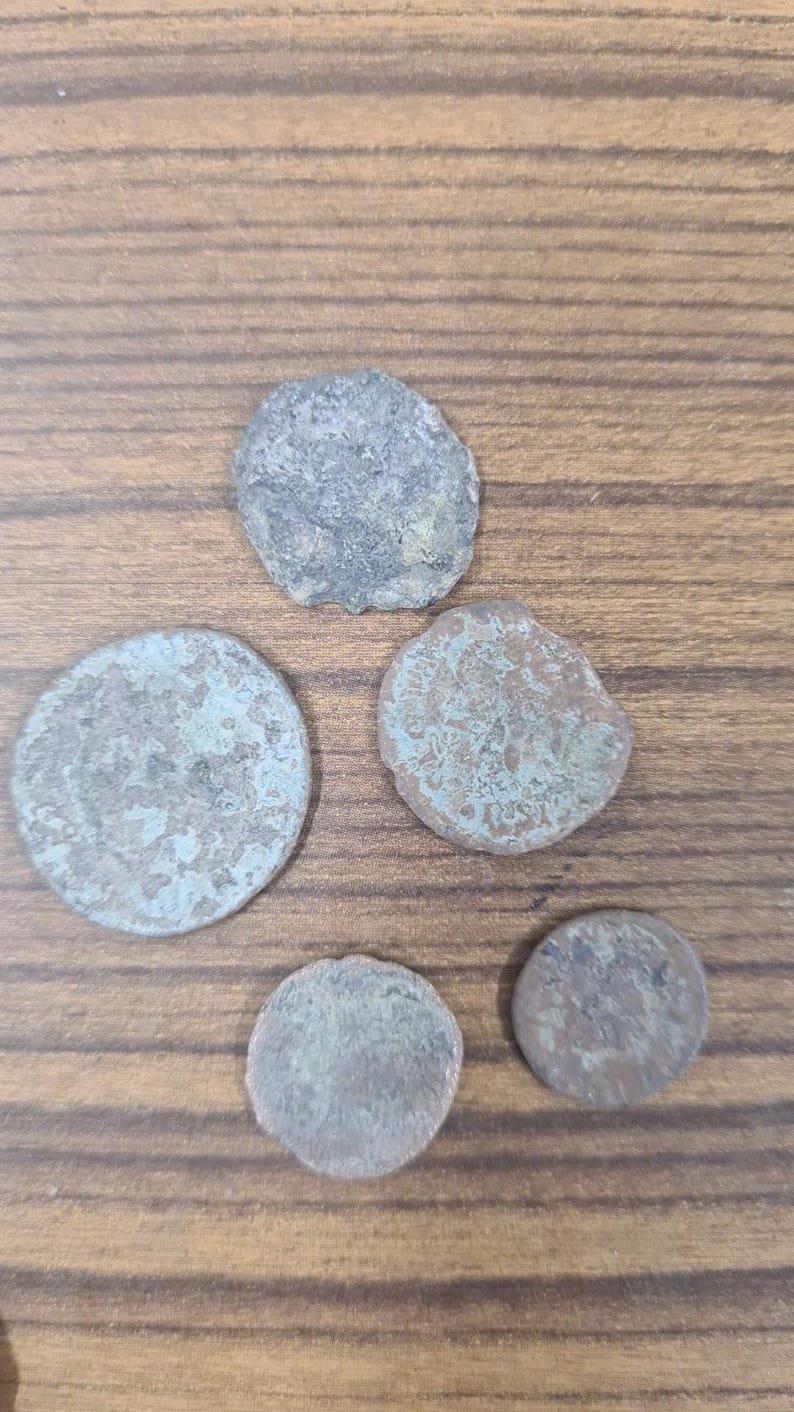 Puede incluir: Cinco monedas antiguas con una p&aacute;tina verdosa sobre una superficie de madera. Las monedas son redondas y tienen un dise&ntilde;o en relieve.