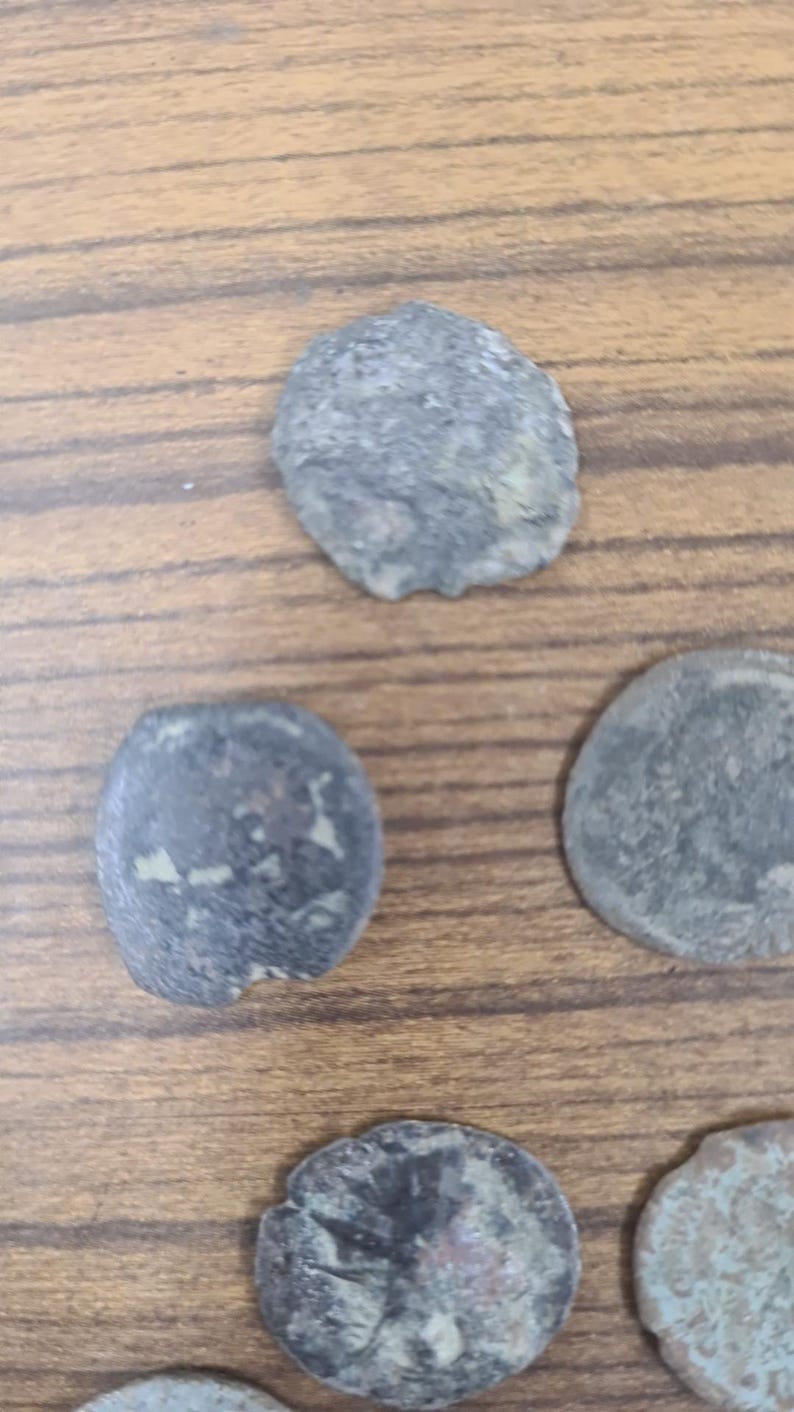 Puede incluir: Una colecci&oacute;n de seis monedas antiguas con un aspecto desgastado y envejecido. Las monedas son de metal oscuro y tienen forma circular. Las monedas est&aacute;n dispuestas en un patr&oacute;n aleatorio sobre una superficie de madera.